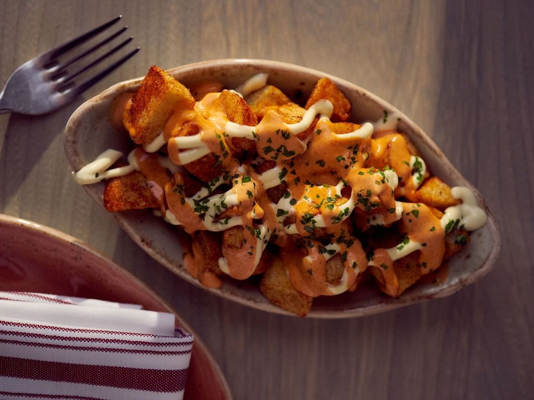 Crispy potatoes with spicy sauce & a bowl by a fork on a wooden table in In-Room Dining at Warwick San Francisco