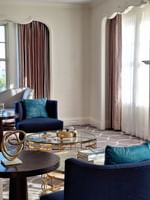 Presidential Suite with Blue velvet armchairs by a gold coffee table under a wall-mounted TV at Warwick Melrose Dallas