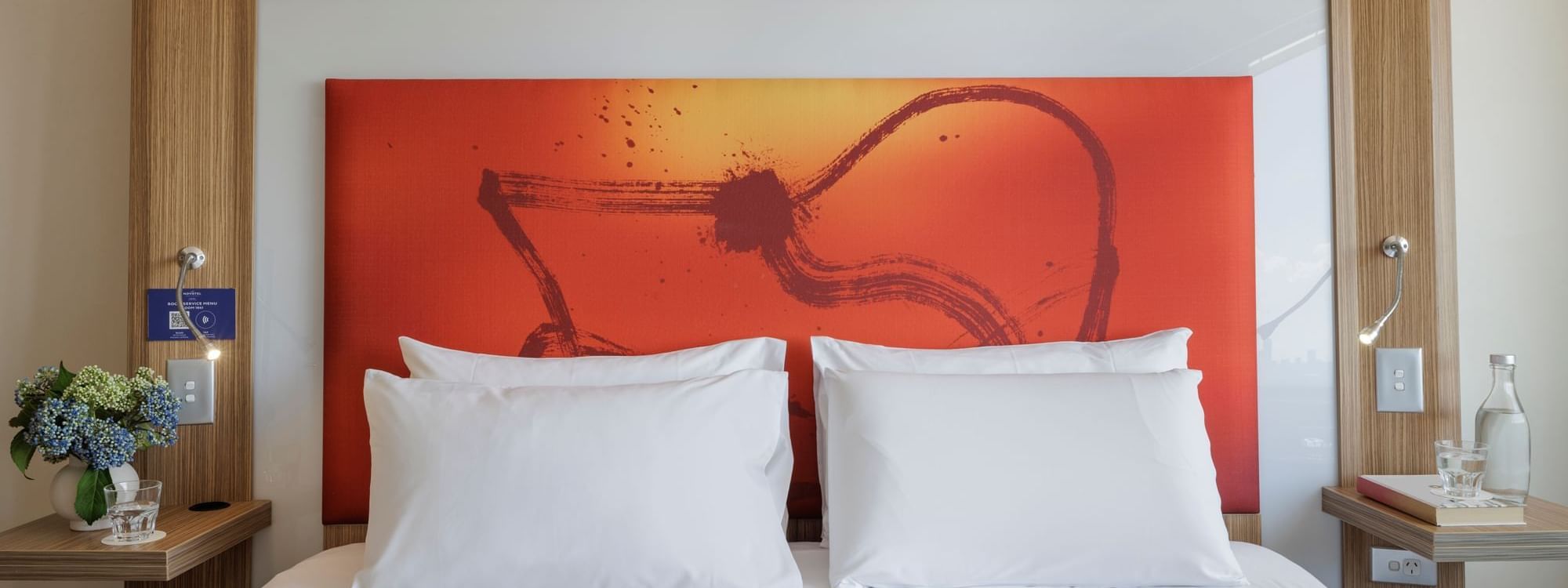 Plush king bed with cushioned headboard and vibrant orange artwork in Superior Spa Suite at Novotel Sydney Olympic Park