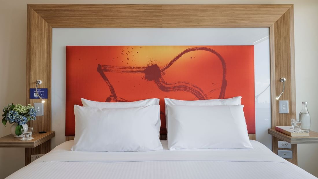 Plush king bed with cushioned headboard and vibrant orange artwork in Superior Spa Suite at Novotel Sydney Olympic Park