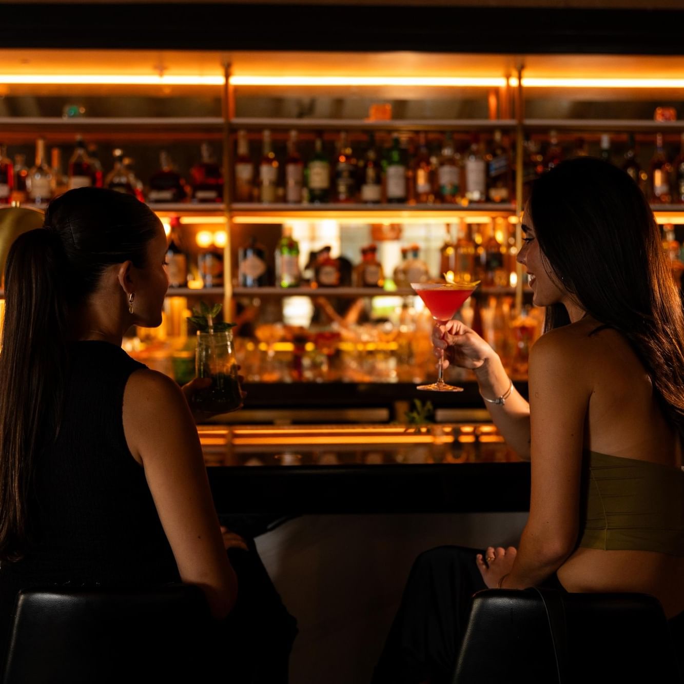 Two women enjoying cocktails at an illuminated bar during Ladies Night