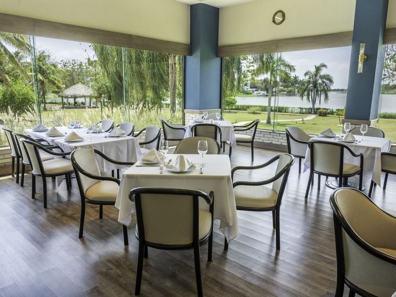 Restaurant with white dining tables, chairs and large windows with garden view at Fiesta Inn Tampico
