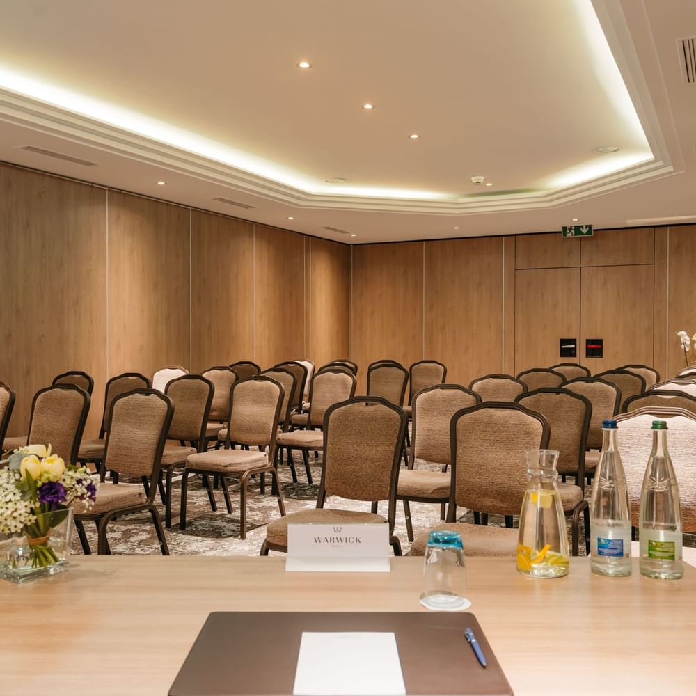 Dent-Blanche with Padded chairs in rows by a wooden speaker desk under a recessed ceiling light at Warwick Geneva