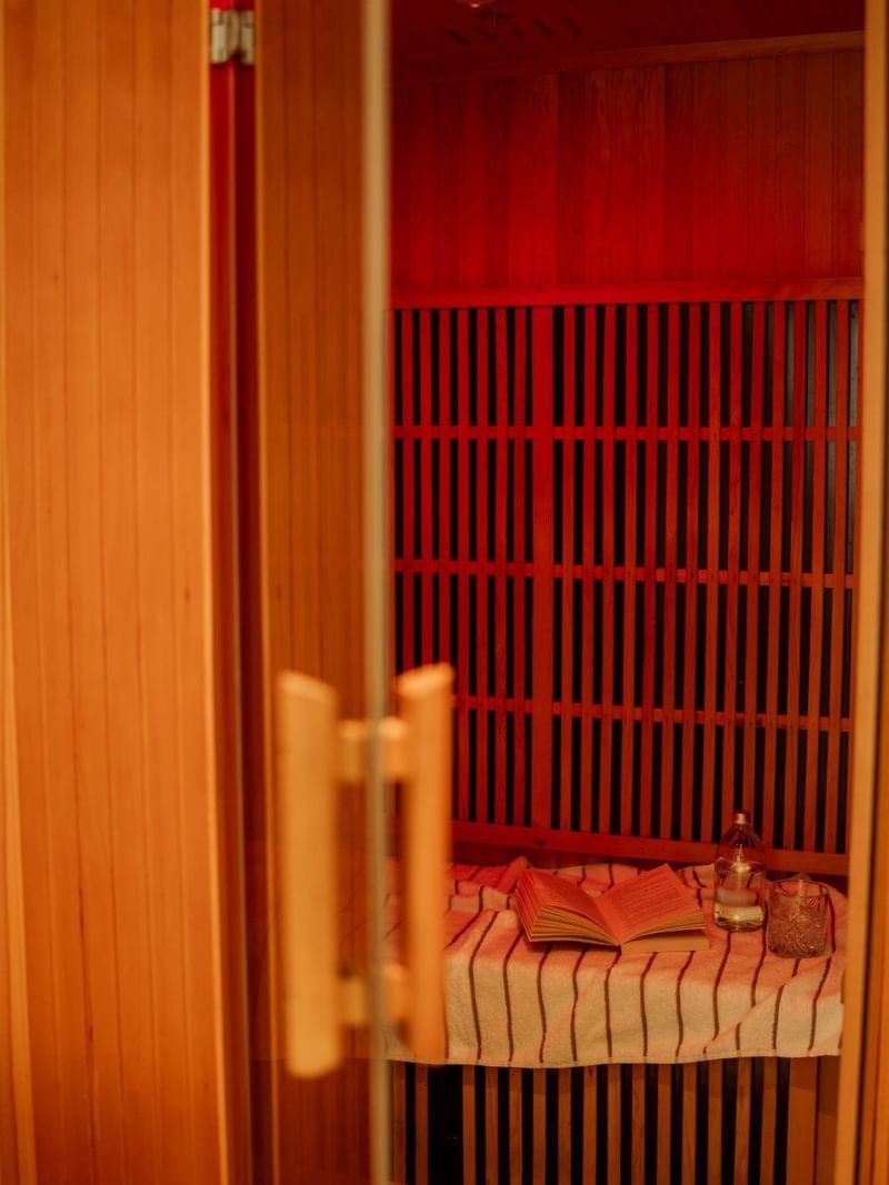 Infrared sauna at Elysium Manly featuring red lights over a book, water bottle, and towel placed by a wooden bench
