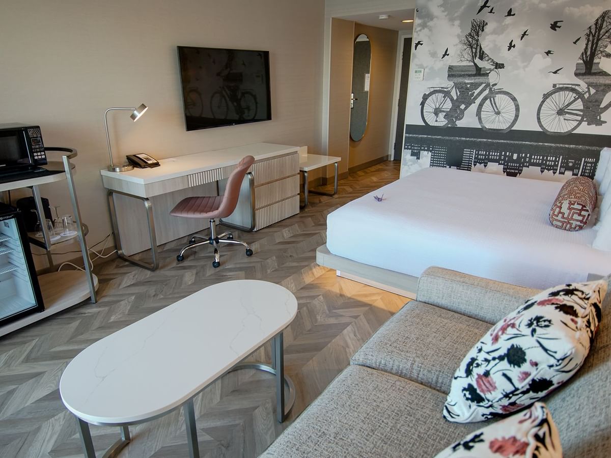 Hotel guestroom with king bed, mini fridge, microwave, coffee maker, couch, coffee table, TV, work desk and chair