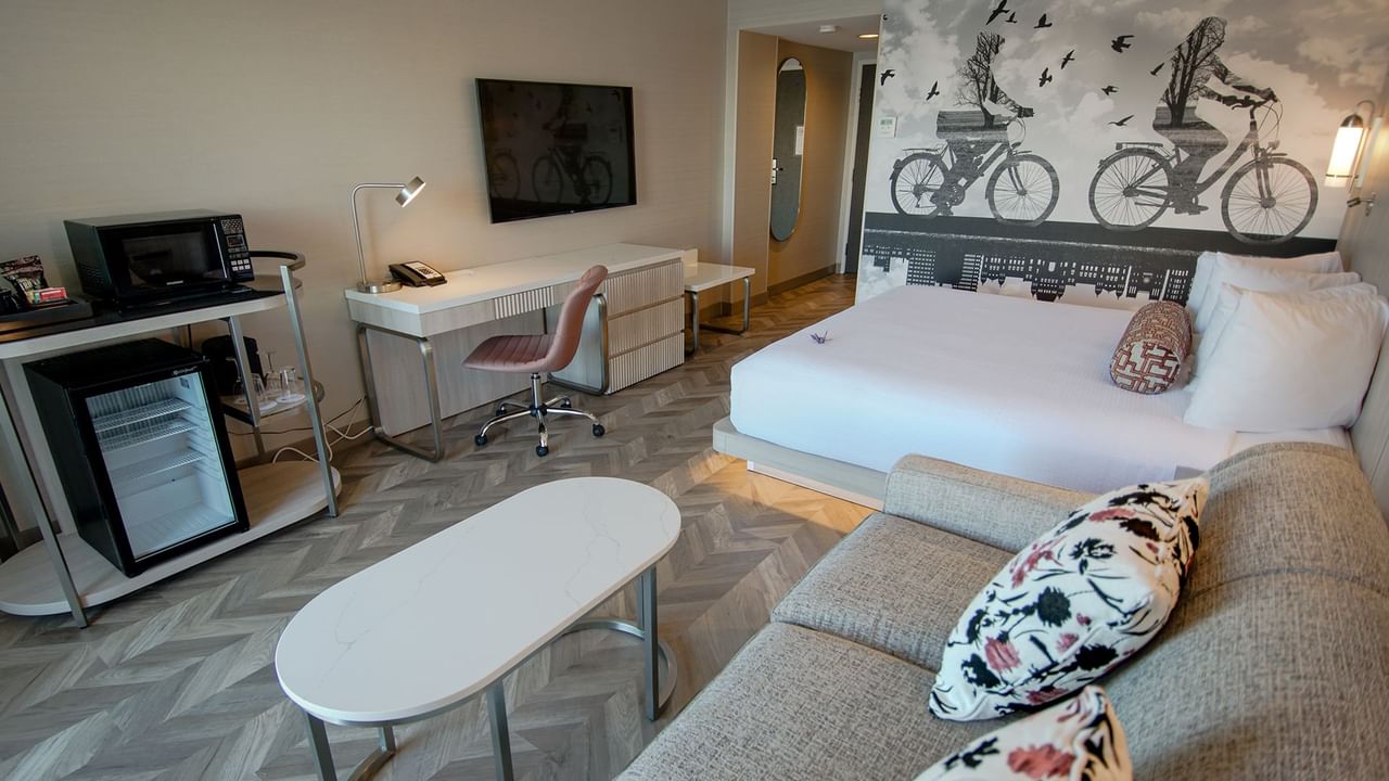 Hotel guestroom with king bed, mini fridge, microwave, coffee maker, couch, coffee table, TV, work desk and chair