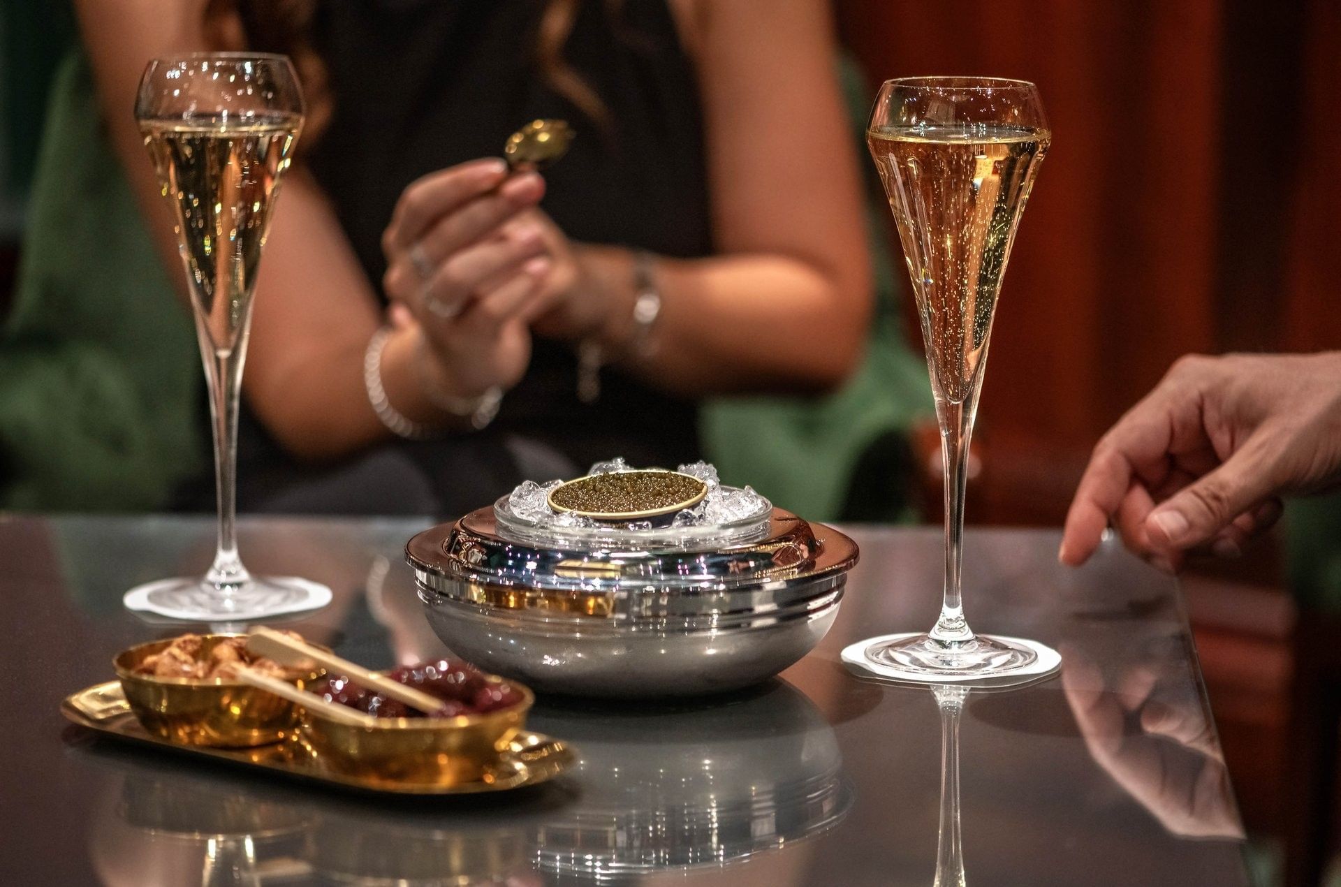 Two flutes of champagne by a bowl of caviar & snacks, held by guests in Duke's Bar at Hotel Westminster Paris