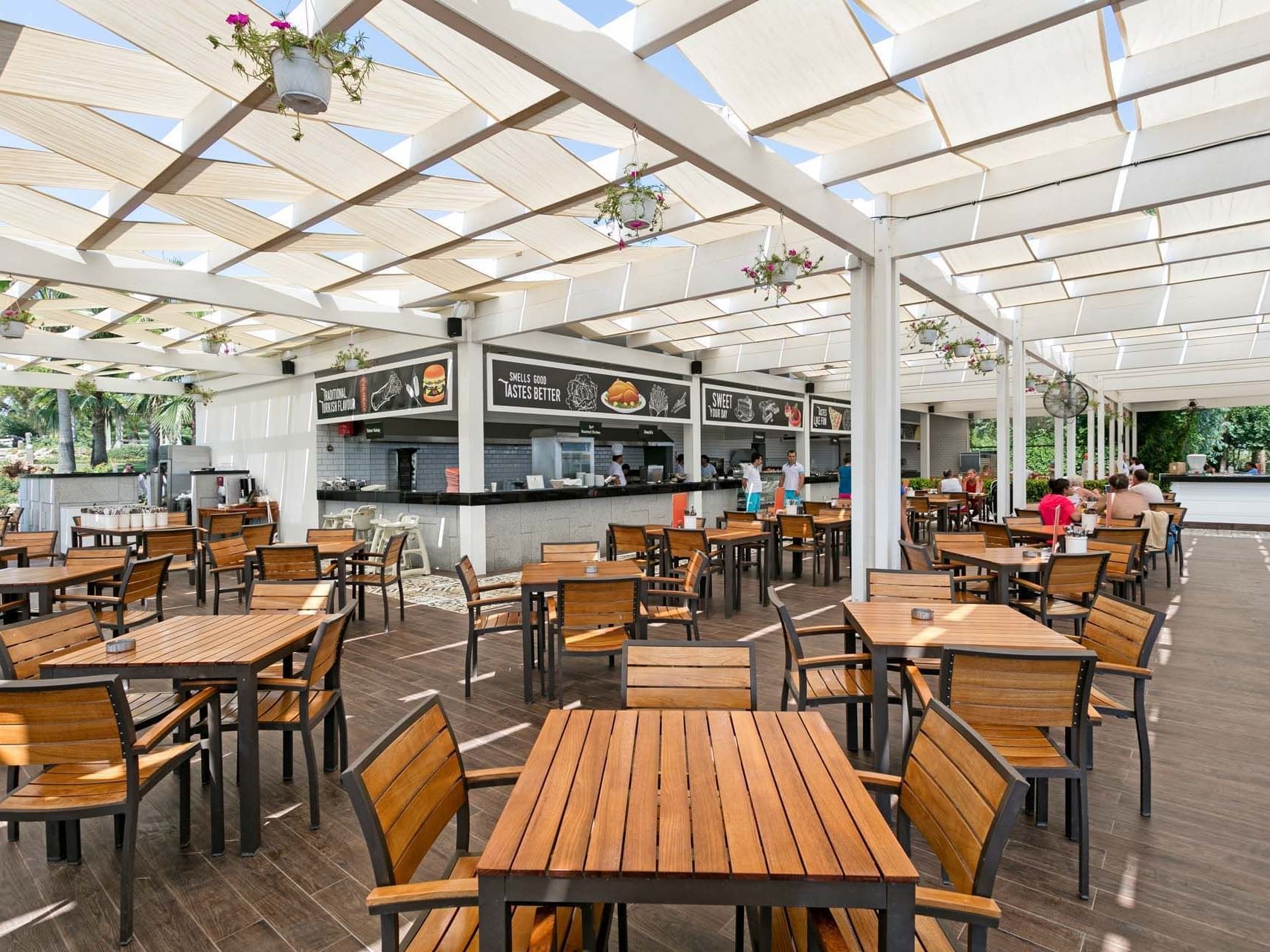 Wooden finished dining tables arranged with chairs in Stella Beach Snack at Titanic Deluxe Lara