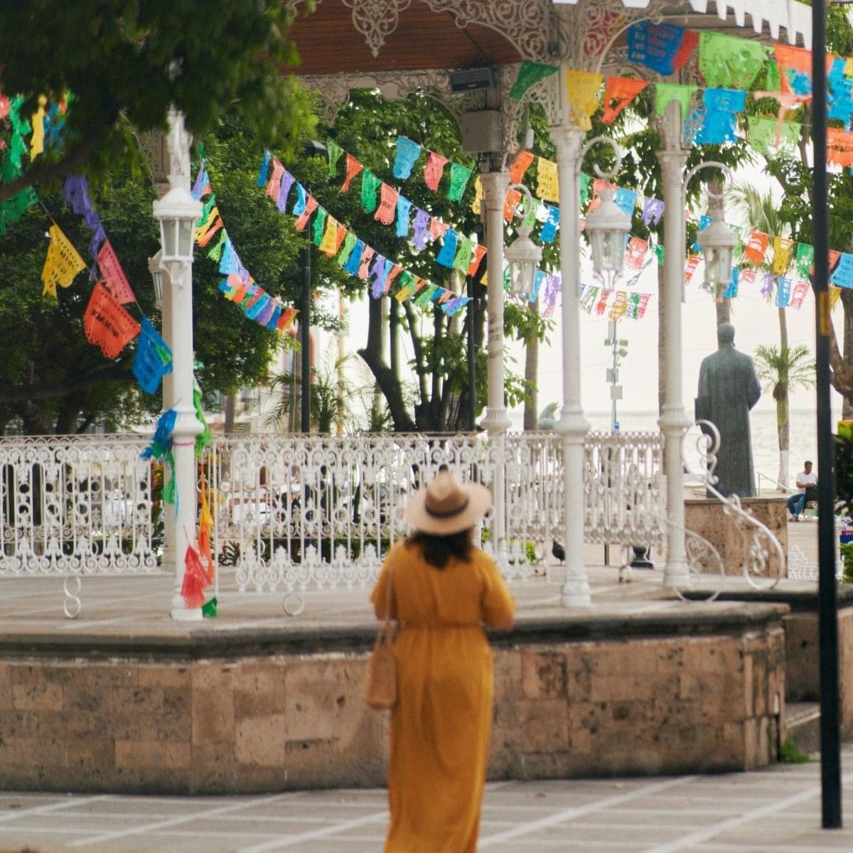 Mujer caminando por la Plaza de Armas en Puerto Vallarta rodeada de colorido papel picado y kiosco tradicional