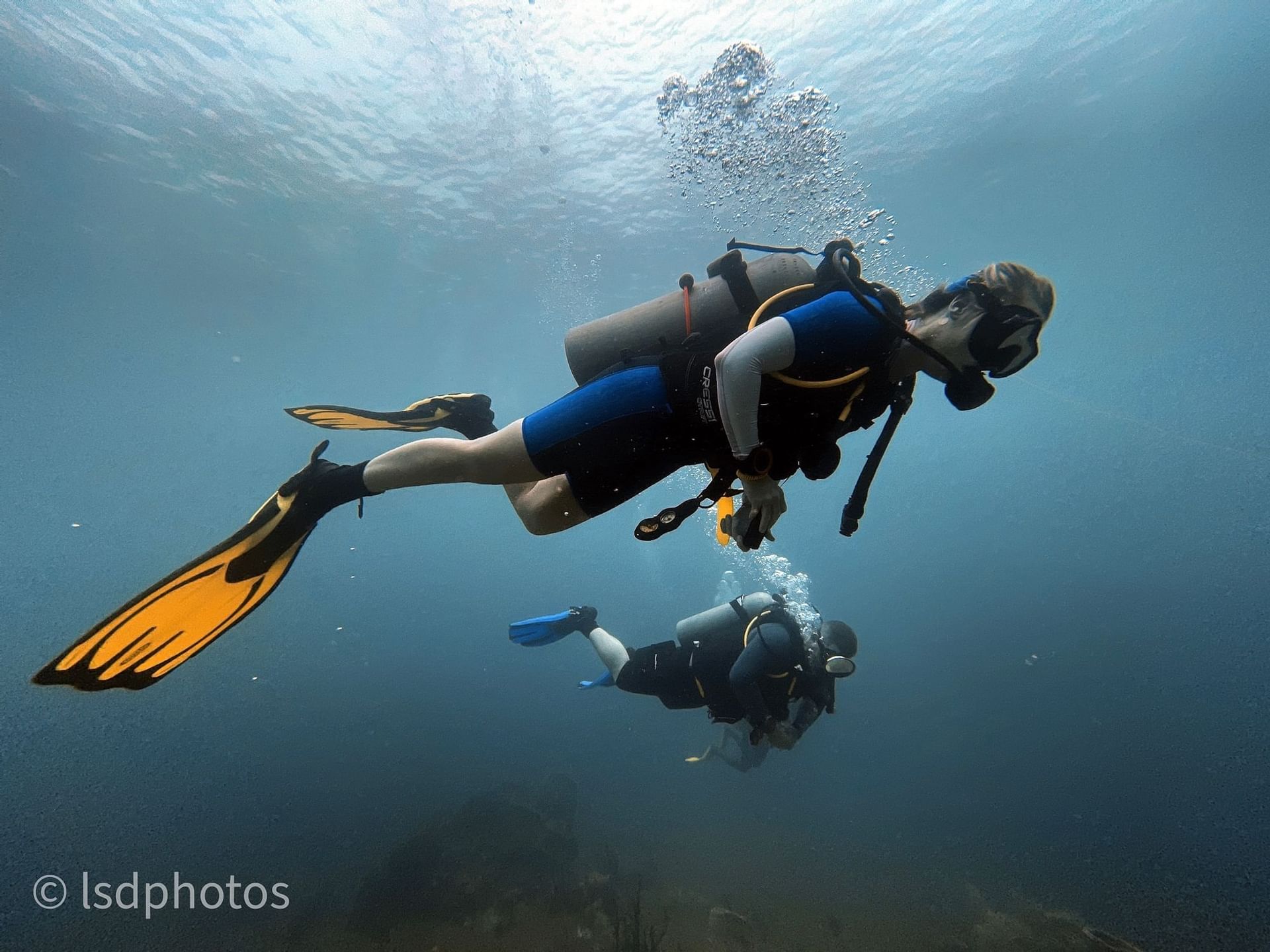 Two divers swimming underwater, surrounded by bubbles and soft blue light near Bay Gardens Hotels and Resorts