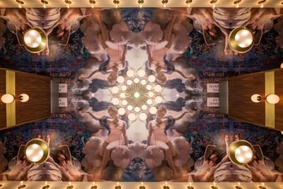Ornate ceiling art with a large painting illustrating a gathering of people in a colorful artistic style at Hotel Bijou