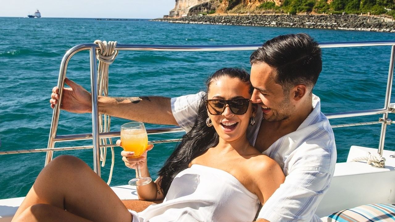 Couple enjoying a luxury sunset catamaran ride with drinks and a scenic view.