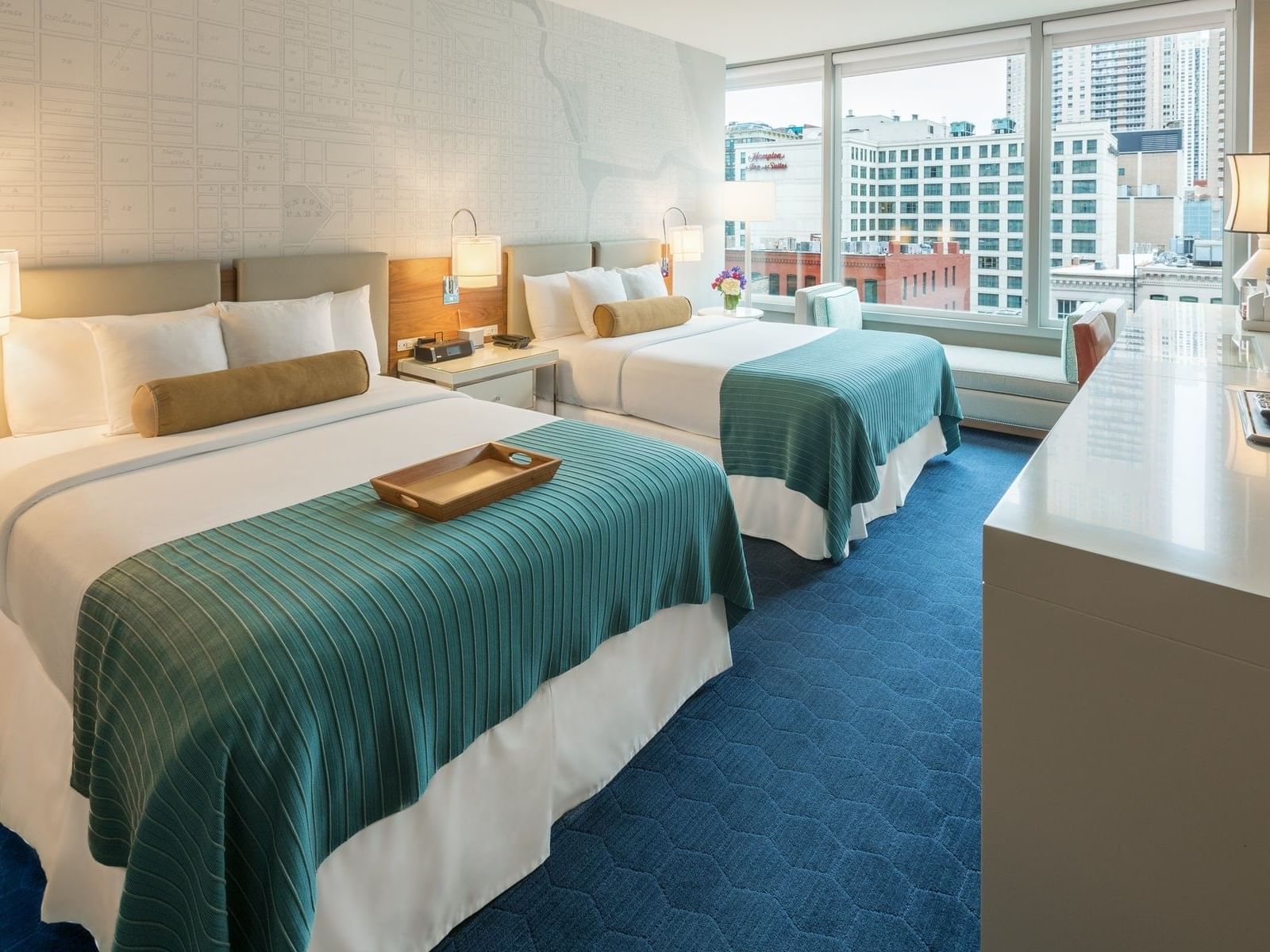 two beds in hotel room with blue carpet and window