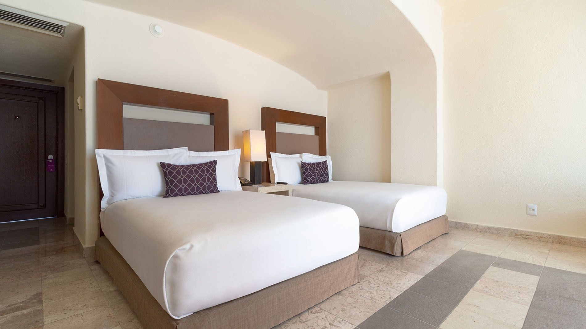 Beds with white linens & purple throw pillows in Partial Ocean View 2 Double Deluxe Room at Camino Real Acapulco Diamante