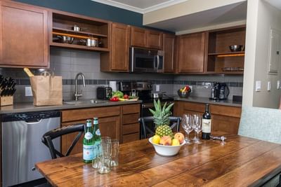 A kitchen at The Stanley Hotel with a wooden dining table, fresh fruit, and a bottle of wine, with a full set of appliances