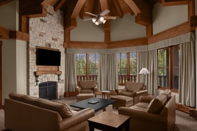 TV lounge with a stone fireplace by large windows with curtains at Hotel Park City Autograph Collection