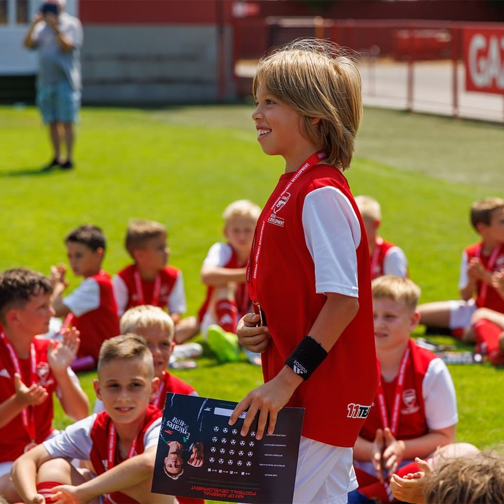 Dijete u sportskom uniformu drži nagradu na Arsenal Football Development Camp.