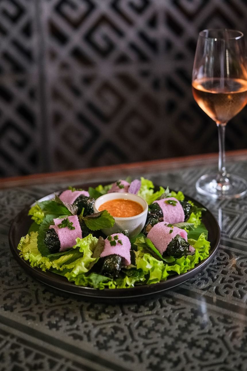 Green lettuce with black rice rolls, pink wraps, dipping sauce, and rosé wine served in 2 Lams Son at Park Hyatt Saigon