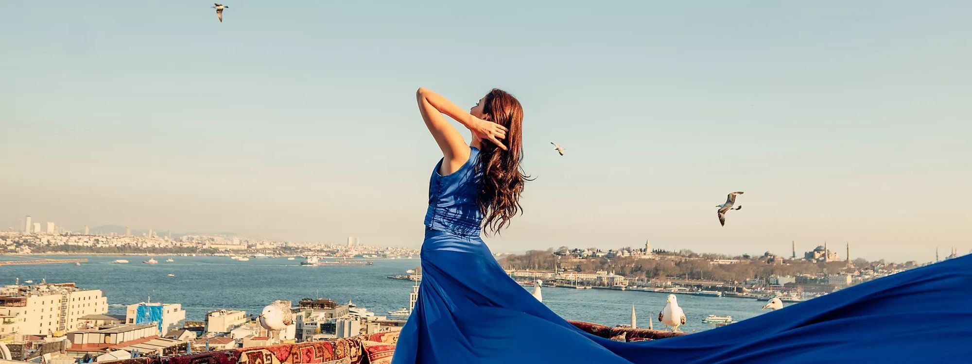 Woman in a flowing blue dress enjoying rooftop views of the city and water near Novotel Sydney International Airport