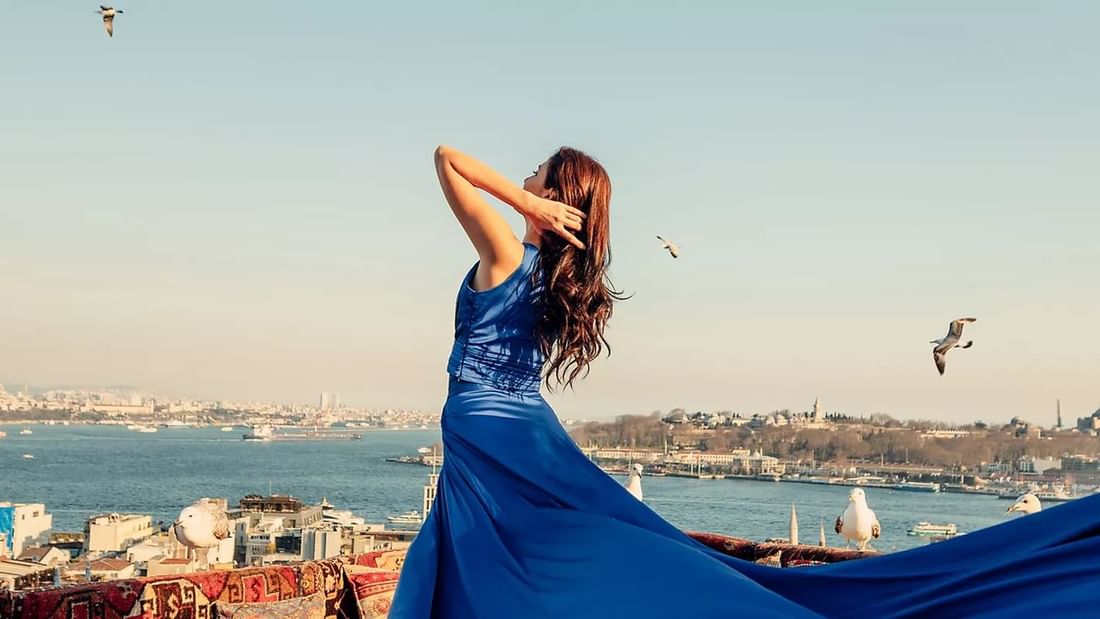 Woman in a flowing blue dress enjoying rooftop views of the city and water near Novotel Sydney International Airport