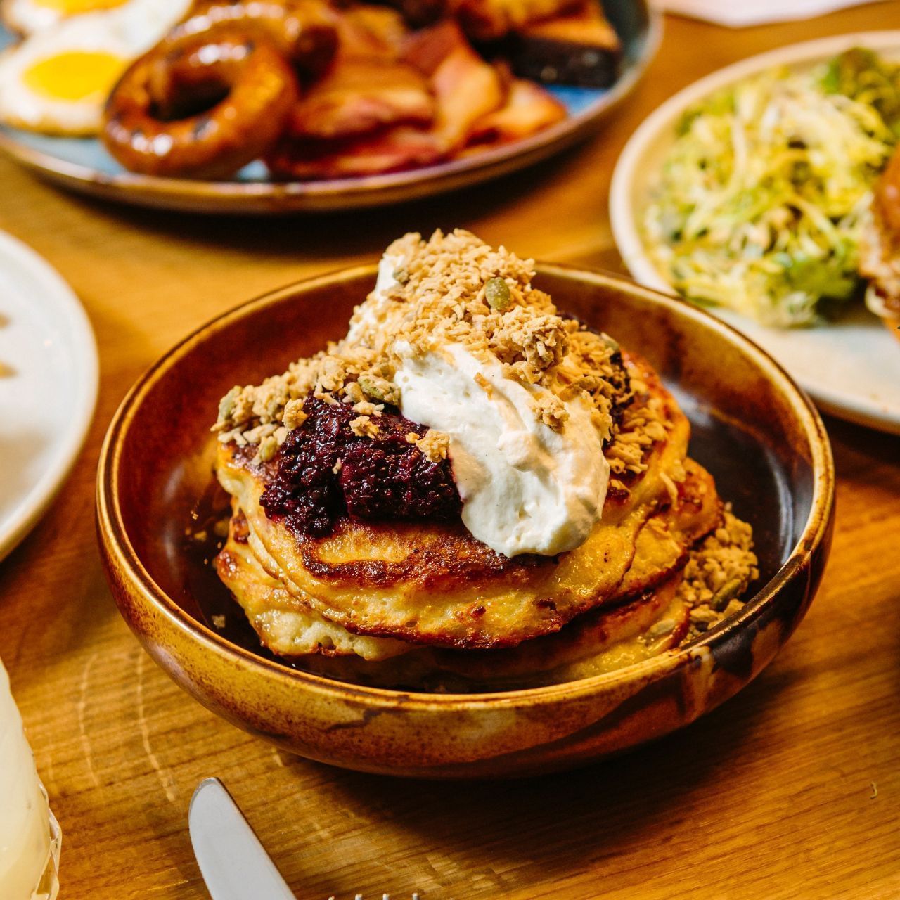 Stack of pancakes topped with berries, whipped cream and crunchy granola served with breakfast dishes at Hotel X Toronto