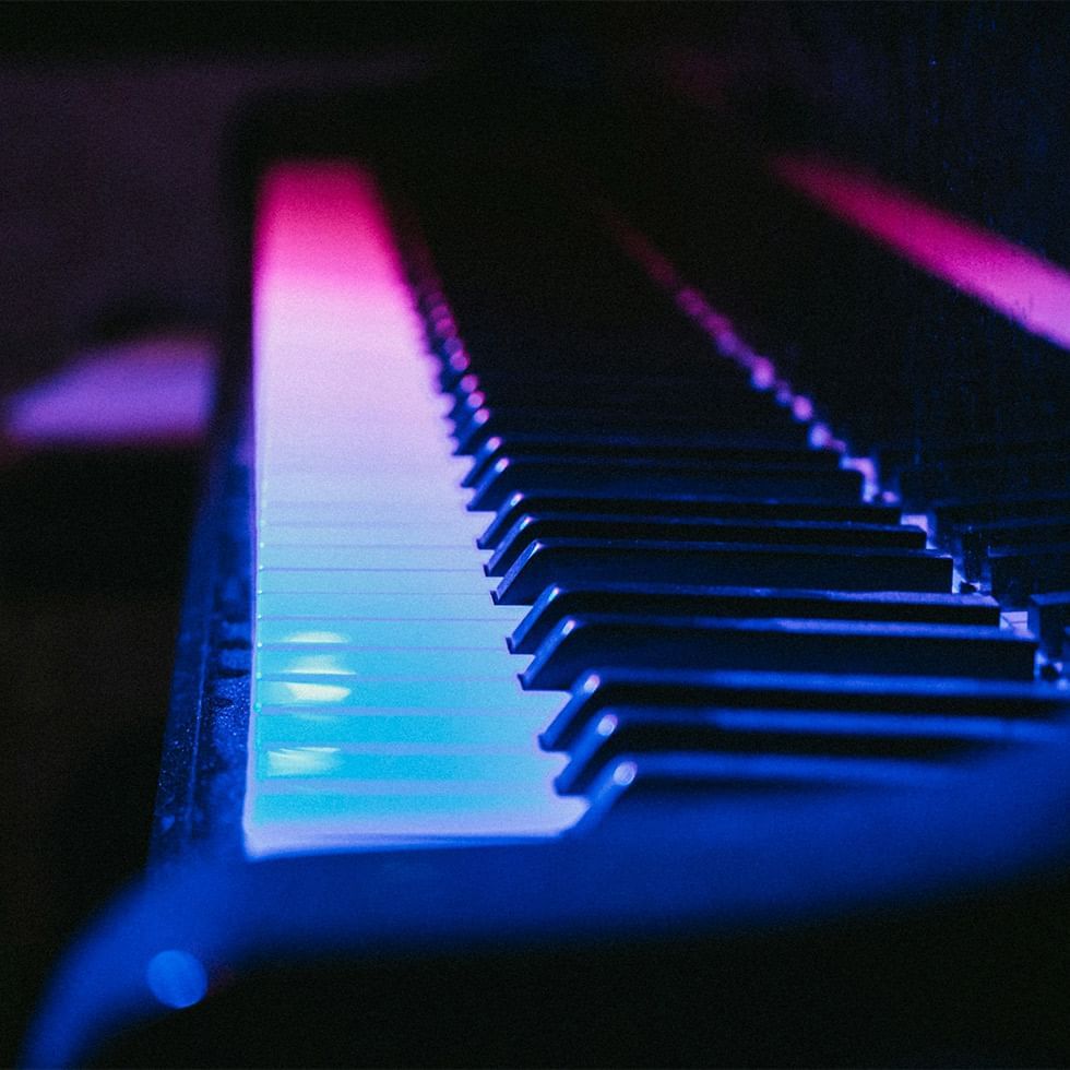 Klaviertasten mit farbigen LED-Lichtern in Blau, Pink und Lila bei schwacher Beleuchtung.