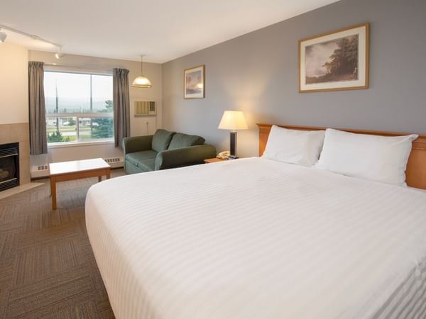 A cozy room with a large bed, green couch, fireplace, window, and framed art.