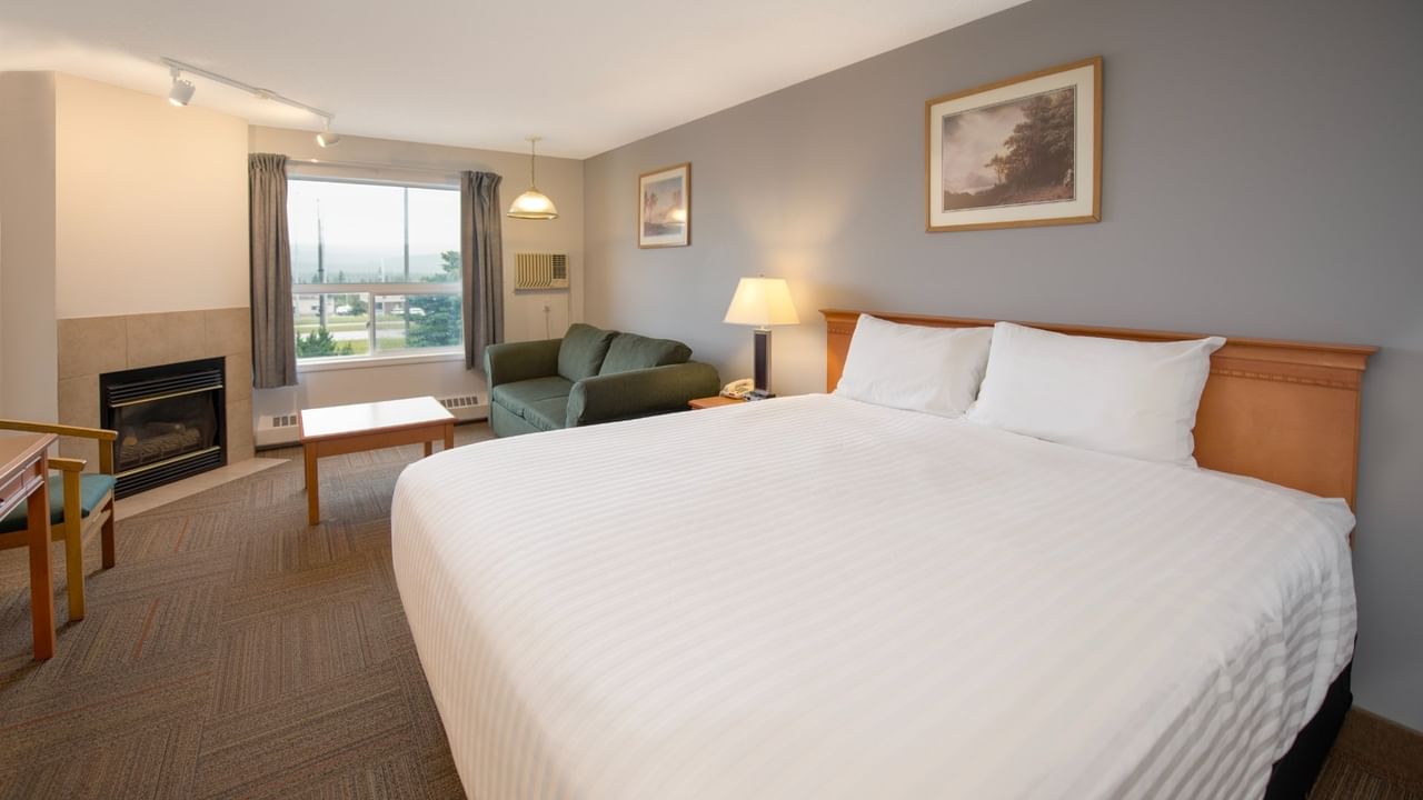 A cozy room with a large bed, green couch, fireplace, window, and framed art.