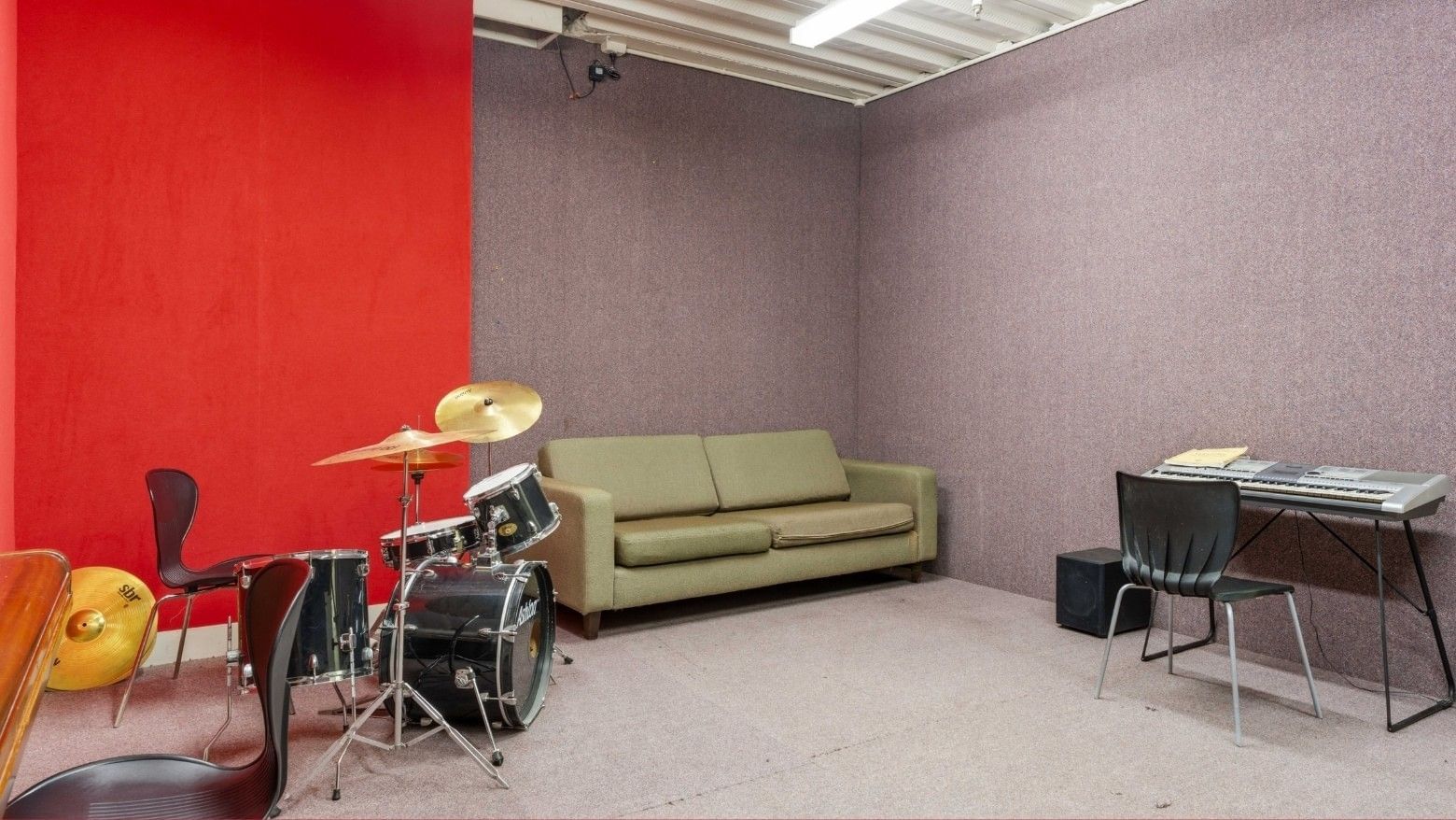 Small room with green couch, drum set, and keyboard setup.