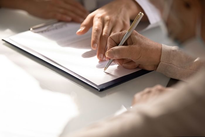 Close-up of a person's hands signing a document on a clipboard with a pen at Buenaventura Grand Hotel and Spa