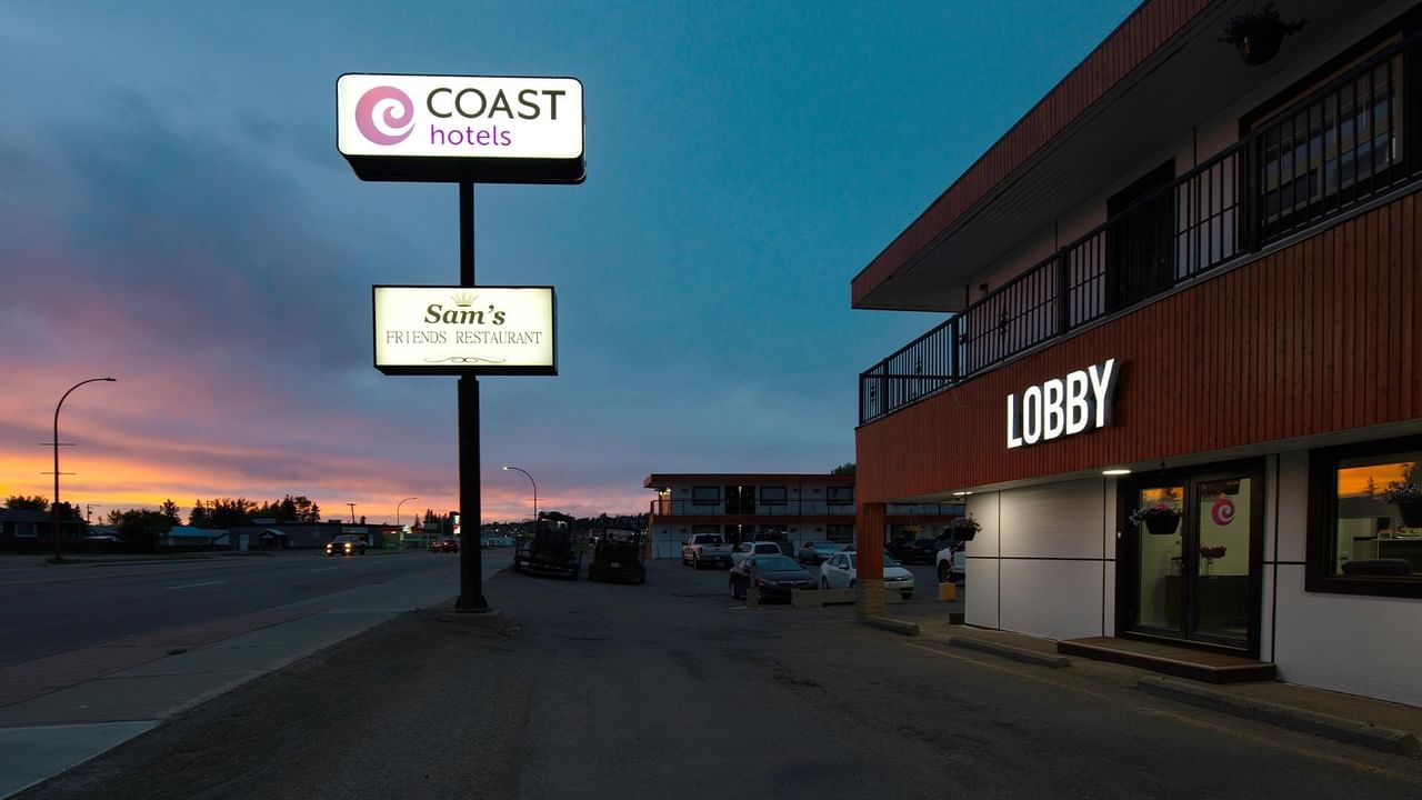 Exterior of Coast Dawson Creek Hotel at dusk, showing the hotel lobby entrance and roadside hotel sign.