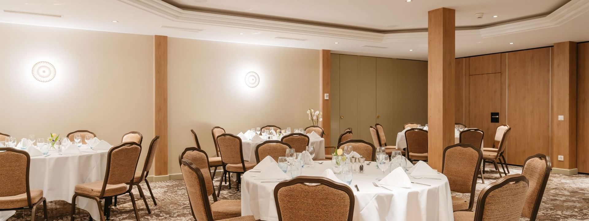 Dining chairs surrounding round linen tables by wooden pillars in Mont-Rose at Warwick Geneva