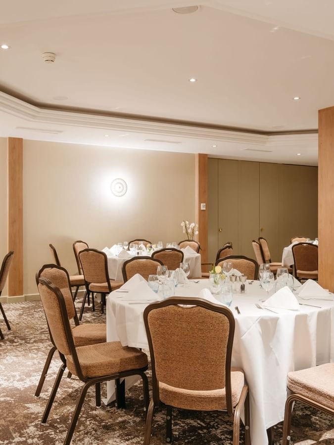 Dining chairs surrounding round linen tables by wooden pillars in Mont-Rose at Warwick Geneva