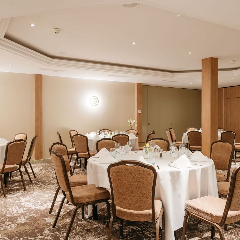 Dining chairs surrounding round linen tables by wooden pillars in Mont-Rose at Warwick Geneva