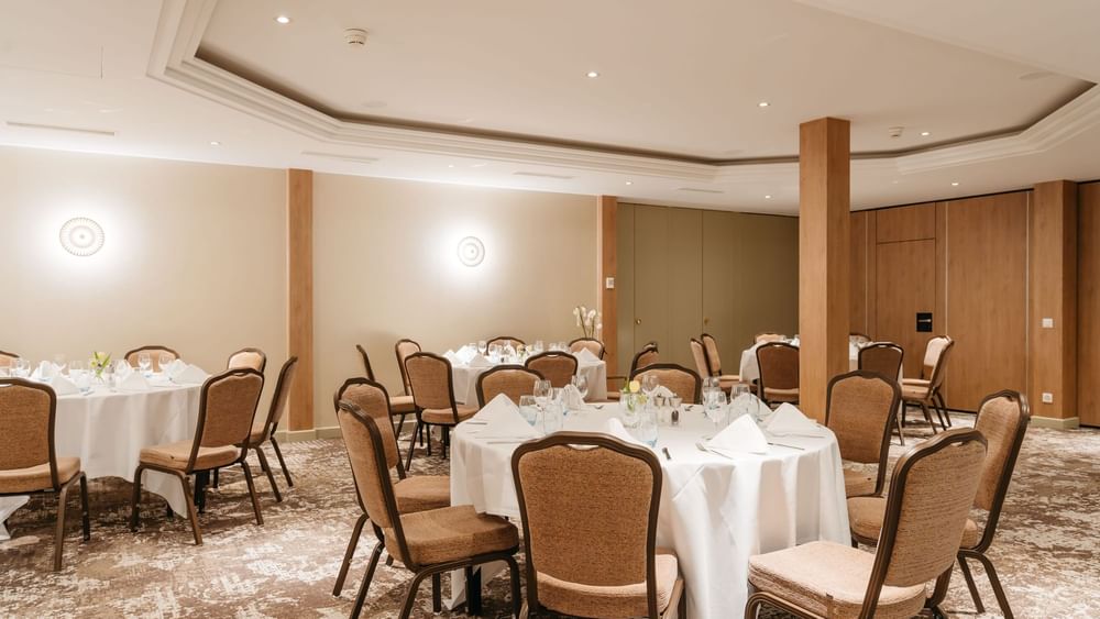Dining chairs surrounding round linen tables by wooden pillars in Mont-Rose at Warwick Geneva
