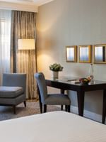 Wooden desk by a gray chair under three square mirrors surrounding a tall floor lamp at Warwick Hotels & Resorts