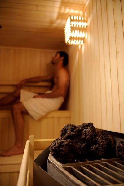 Piedras de sauna caliente junto a pared de madera bajo luz cálida cerca de un huésped en Noi Spa de NOI Vitacura