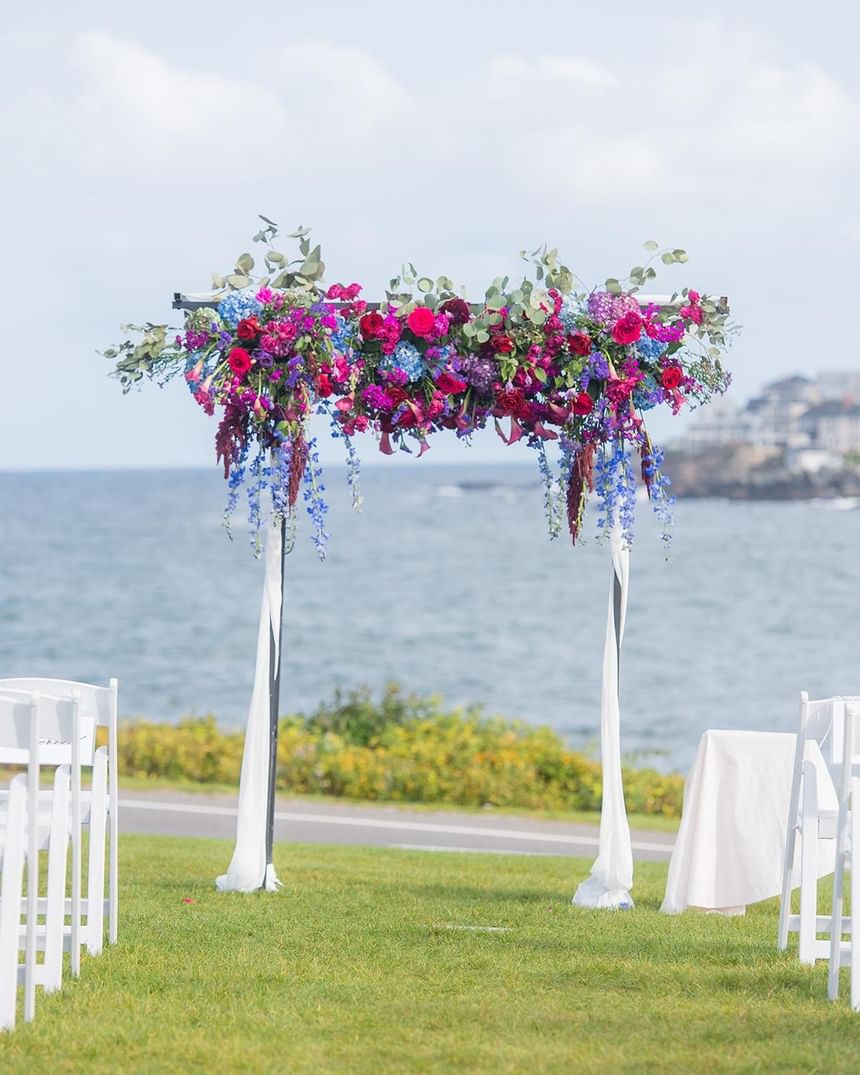 Floral wedding arch arranged outdoors with a sea view at Ogunquit Collection