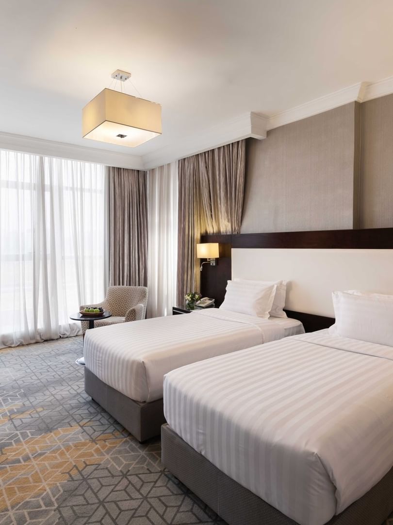 Work desk, nightstand, and cozy lounge chair by the beds in the Deluxe Room at Warwick Hotel Jeddah