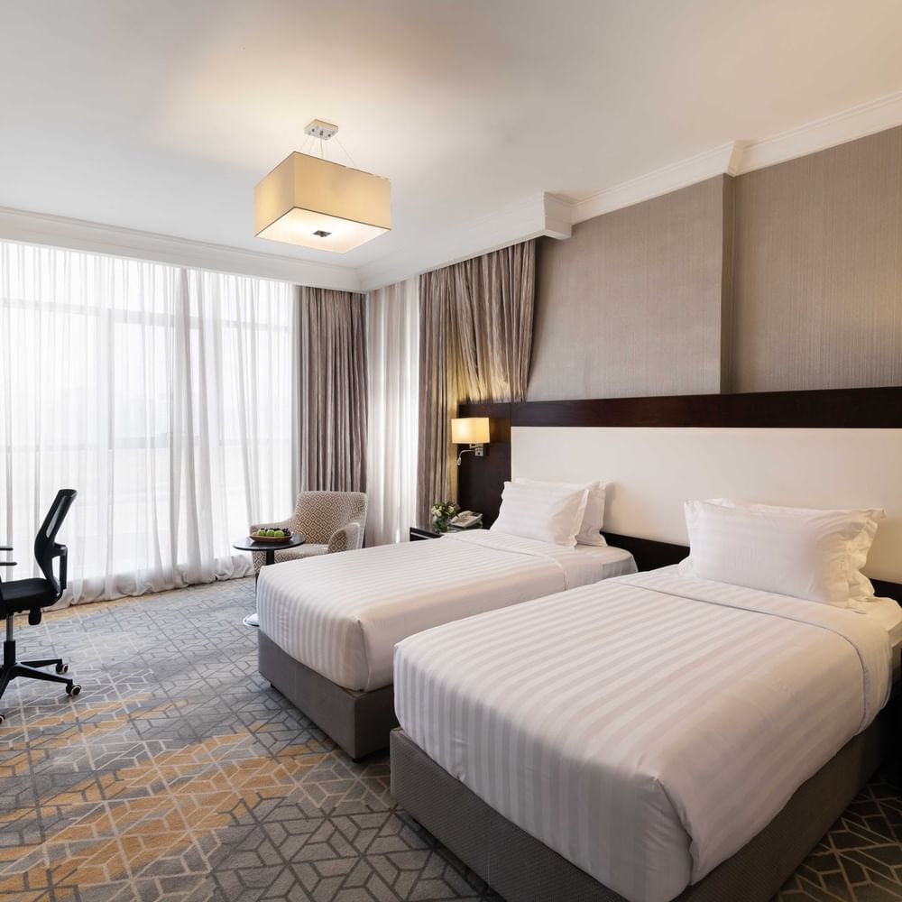 Work desk, nightstand, and cozy lounge chair by the beds in the Deluxe Room at Warwick Hotel Jeddah