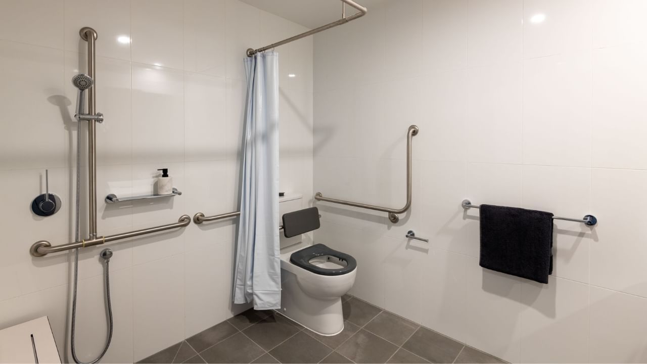 White accessible bathroom with grab bars, shower, toilet, and towel rack.