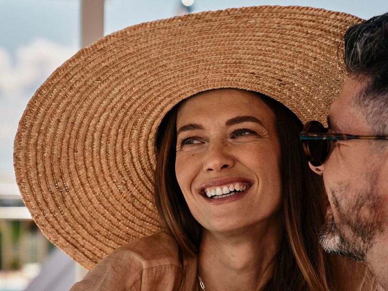 Close-up of woman wearing a hat & laughing with someone at Falkensteiner Hotel & Spa Carinzia