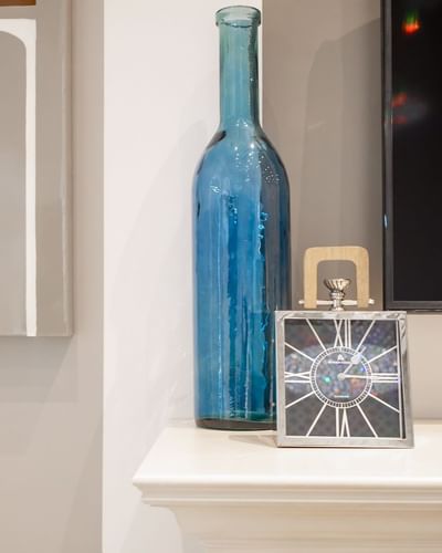 A decorative blue bottle and silver analog clock on the mantelpiece in Presidential Suite at Retro Suites Hotel