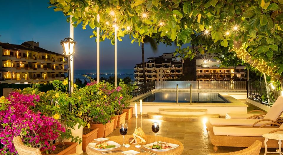 Dinner table with wine by rooftop pool and blooming pink bougainvillea under lit trees at Casa Dona Susana
