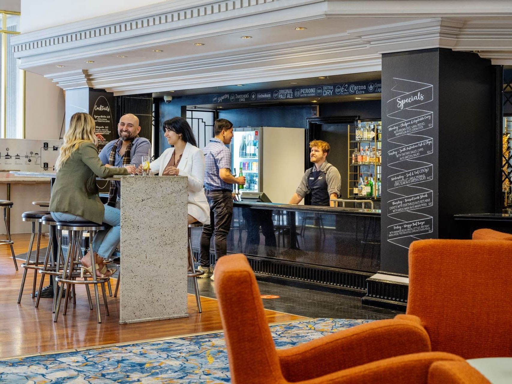Three people enjoying drinks while having a conversation in front of the counter in bar at Hotel Grand Chancellor Adelaide