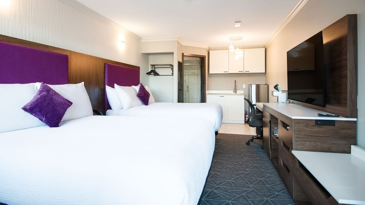 Hotel guest room with two queen beds, a kitchenette, flat screen TV, and work desk