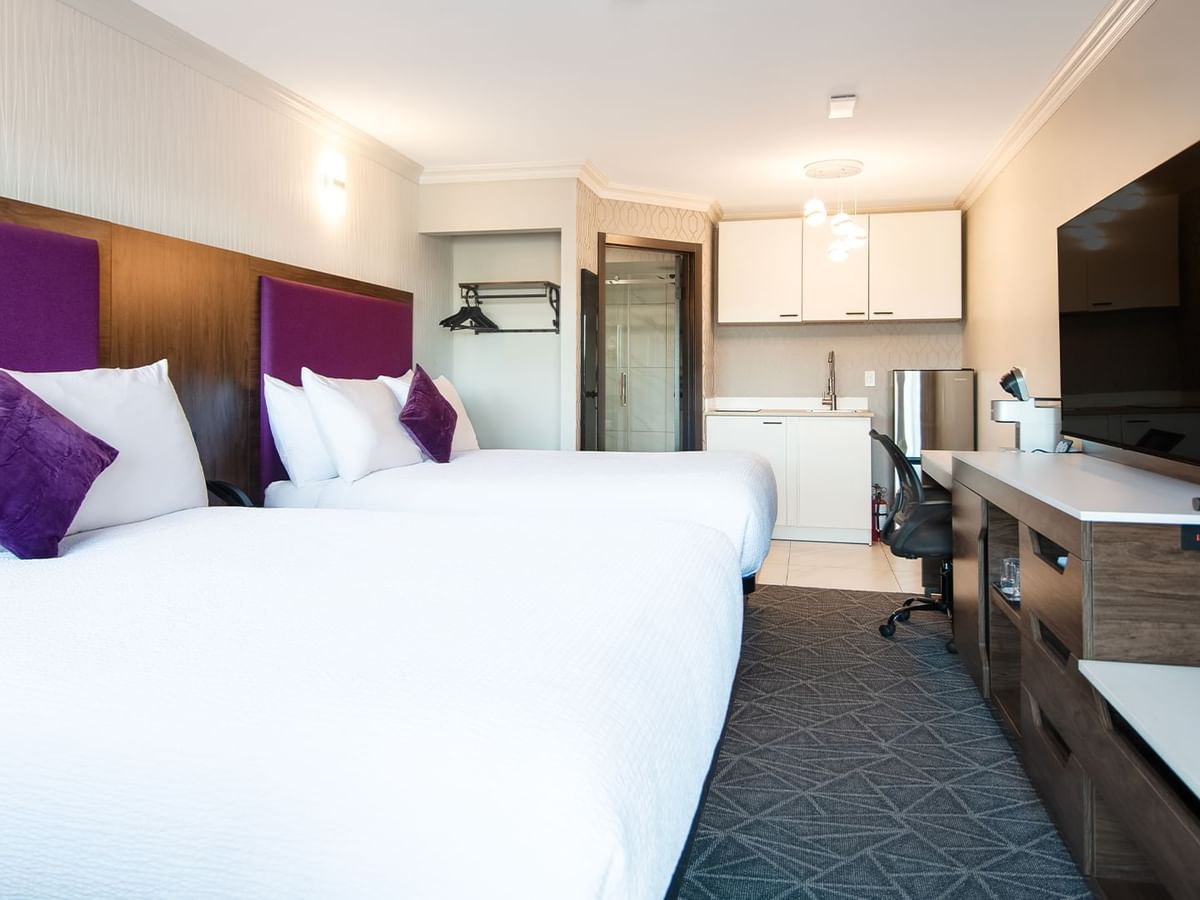 Hotel gust room with two queen beds, flat screen TV, kitchenette, and work desk