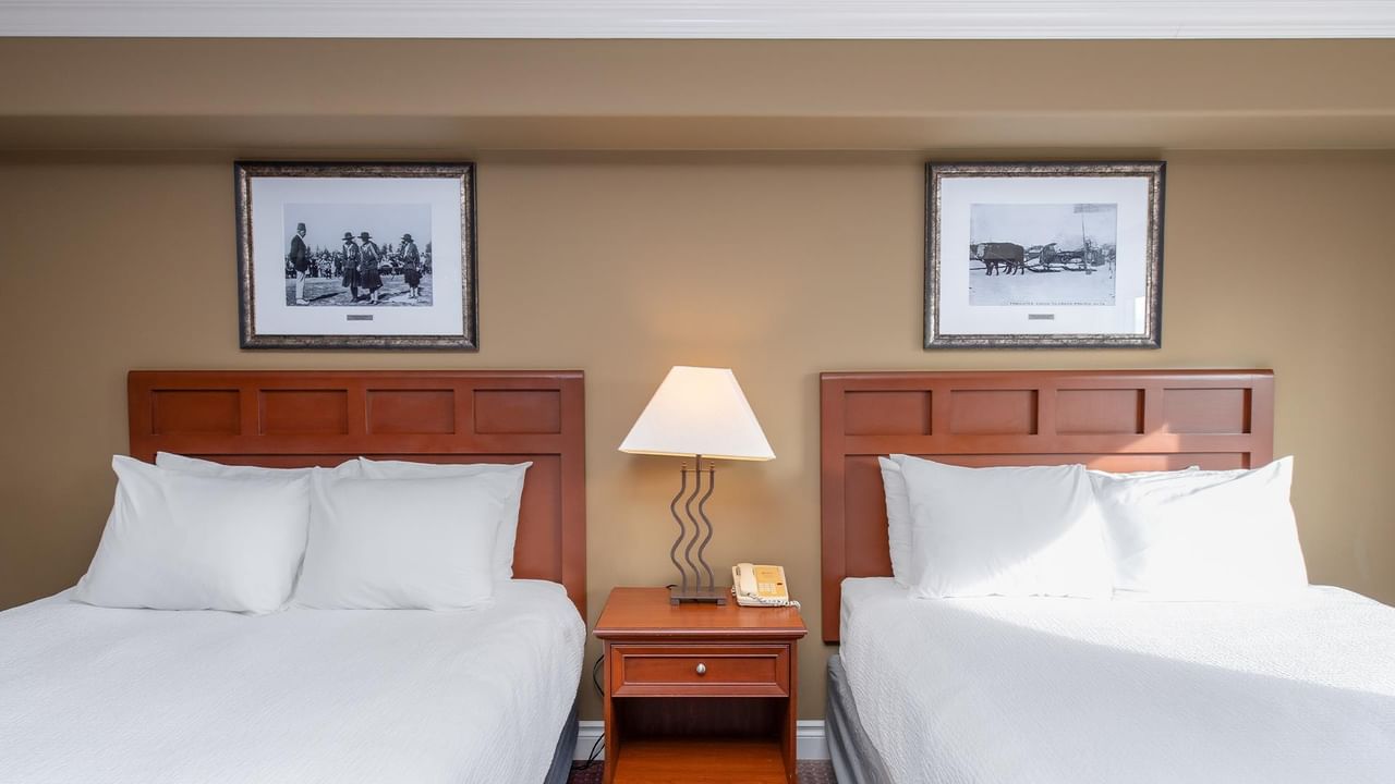 Two double beds with white linens, wooden headboards, and vintage photographs above at Coast Edson Hotel.