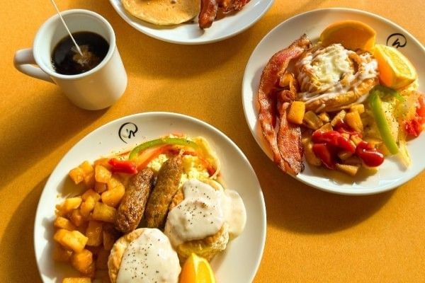 An overhead shot of three full plates of breakfast food and creamer being poured into a mug of coffee at the breakfast buffet at Rosen Inn International.