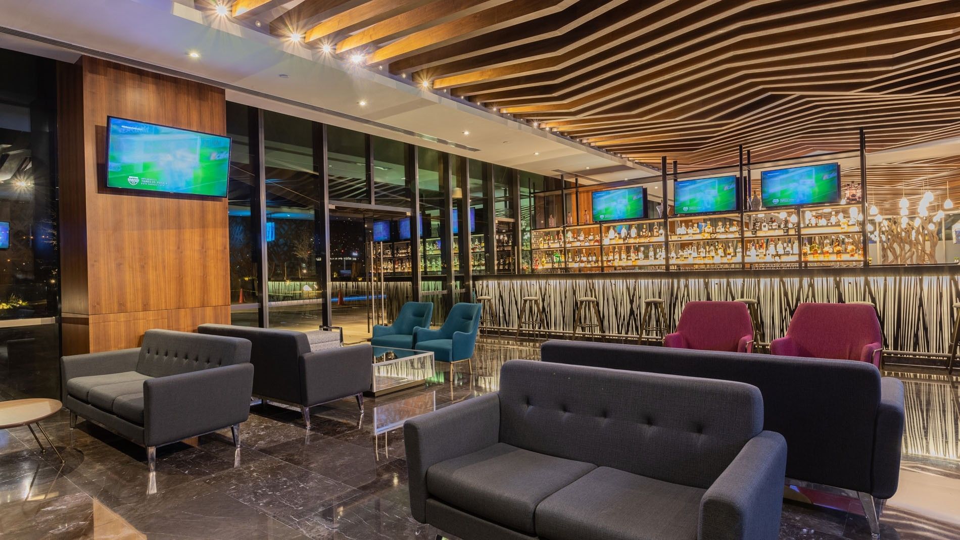 Blue bar lounge with a view of the spirits back-bar and plush armchairs at Camino Real Fashion Drive, Monterrey
